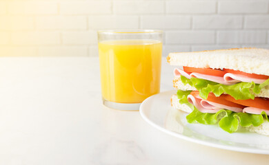 Sandwich and orange juice on white table. European breakfast