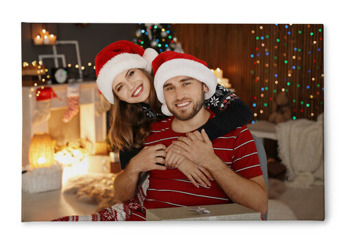 Photo printed on canvas, white background. Happy young couple in Santa hats celebrating Christmas at home
