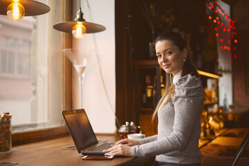 Young girl works in a cafe on a laptop performs customer work remotely.