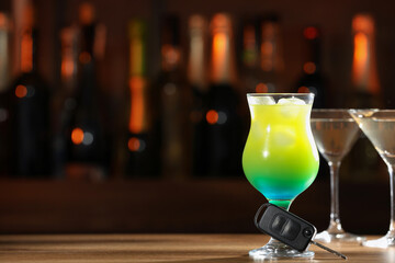 Car key and glass of alcoholic drink on table against blurred background, space for text. Drunk driving concept
