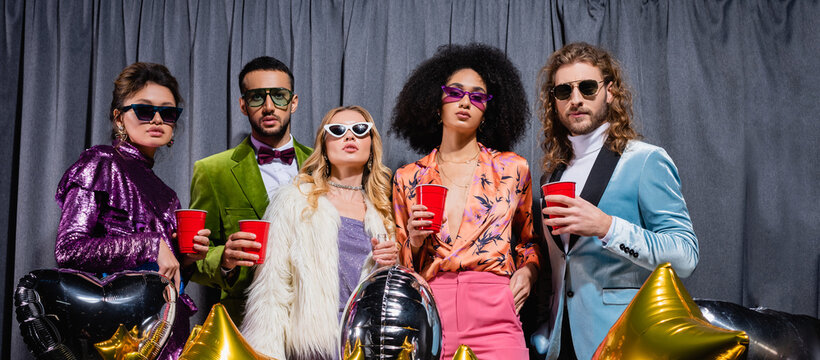 glamorous interracial friends standing on grey background, banner.