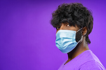 African american man wearing medical face mask against purple background
