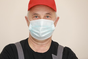 Work are done. Portrait of worker man with medical mask in red overall, black t shirt , red cap looking in camera. white background, indoor studio shoot isolated.