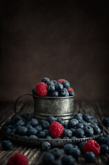 Blueberries and raspberries in a vintage cup on a dark background. Photo in Rustic style. Copy space. High quality photo