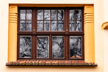 Art Nouveau window. Brown window frame at yellow vintage building. Historic window at Riga, Latvia, Europe. Trees are reflecting in dark antique window at yellow facade