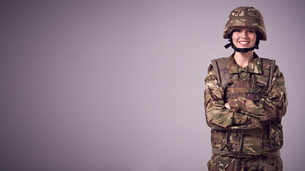 Studio Portrait Of Smiling Young Female Soldier In Military Uniform Against Plain Background