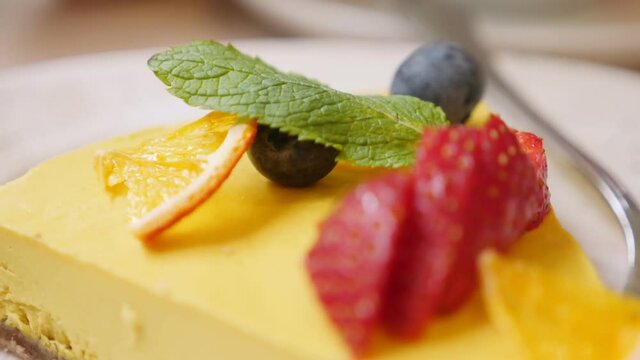 closeup of a slice of raw mango passionfruit cake garnished with strawberries and blueberries.