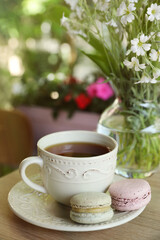 Cup of  drink, macarons and flowers on table outdoors in morning