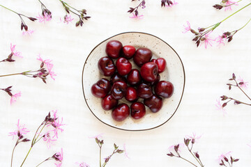 Cherries in a plate on a white tablecloth and wildflowers, flat lay.