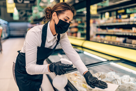 Young employee with face protective mask disinfecting surfaces at grocery store.
