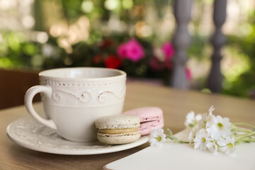 Cup of drink, macarons and flowers on table outdoors in morning