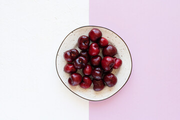 Cherries in a plate on a white and light violet background, flat lay.