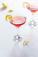 Cosmopolitan cocktail served with lemon wedges on a white background