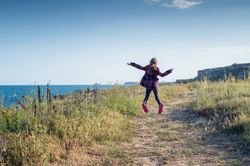 Happy little girl jumping and enjoying life on a spring path along picturesque coastline