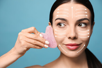 Beautiful young woman doing facial massage with gua sha tool on blue background, closeup