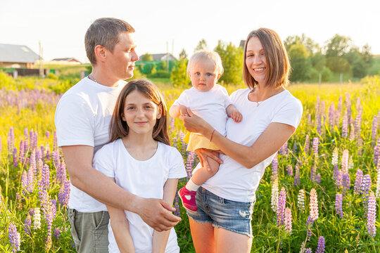 Happy Family Mother Father Embracing Kids Outdoor. Woman Man Baby Child And Teenage Girl On Summer Field With Blooming Flowers Background. Happy Family Mom Dad And Daughters Playing On Meadow.