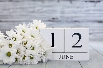 
White wood calendar blocks with the date June 12th and white daisies. Selective focus with blurred background.