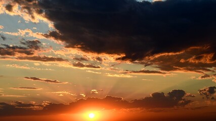 Shiny golden sun rays break through dark clouds. Orange color cloudscape of sunset. Dramatic sky while sundown in dusk