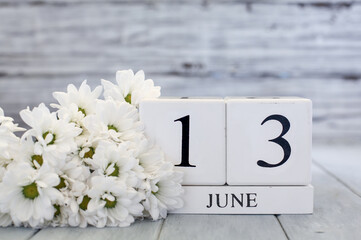 White wood calendar blocks with the date June 13th and white daisies. Selective focus with blurred background.