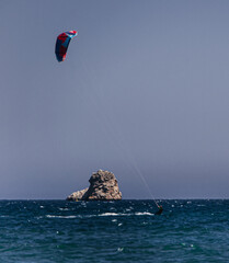 person kitesurfing in the medes islands, windy day with clear blue sky and a bit busy sea, composition of three objects in a diagonal line, sailing, little island, person