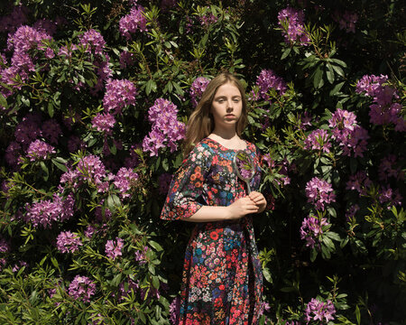 Girl in flowerdress standing near rhododendron flower bush