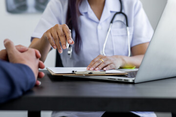 Close up of doctor  and patient taking, doctor working with laptop computer and writing on paperwork. Hospital background.