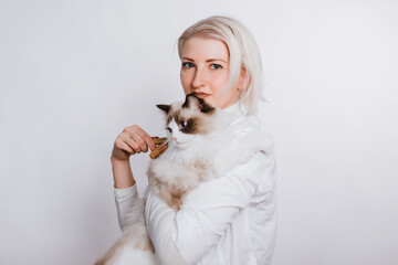 A girl in a white coat is holding a fluffy cat regg dol. Veterenar is combing the animal.