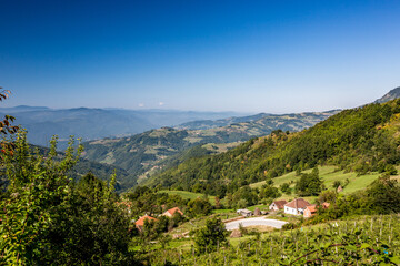 Fototapeta na wymiar Countryside mountain hill view of a small village, Western Serbia, travel photo from a road close to Montenegro. Clear blue sky and vivid green colors