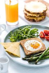 Sunny side up egg in a toast served with cheese, asparagus, rocket and tomatoes on a rustic white background