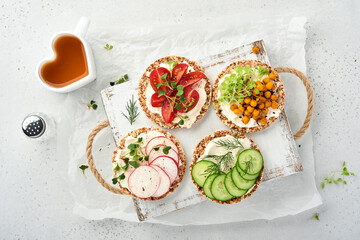 Four crispy buckwheat bread with cream cheese, radish, tomato, chickpea, cucumber and microgreen for healthy breakfast on parchment paper on grey stone background. Concept vegan and healthy eating.