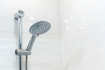 Shower head on a background of white, ceramic tiles. Copy space