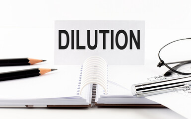 Text DILUTION on paper card,pen, pencils, glasses,financial documentation on table - business concept