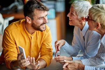 Two older business women of similar appearance are interested in a story from young male colleague...