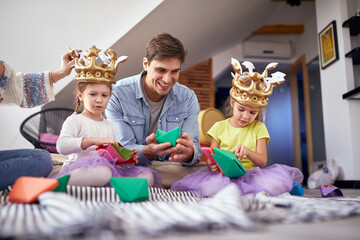 A young family sitting on the floor at home and playing with paper boats. Family, together, playtime, home