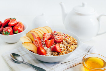 breakfast porridge oatmeal with cereal granola strawberries peaches honey in a white plate on the background of a white teapot and bowls with honey on a white plate