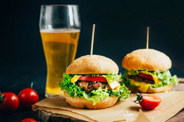 close-up of a hamburger with meat on a grill tomato and greens on the background of a glass with beer on a black background