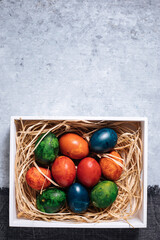 Easter eggs in box with golden hay on a rustic plain grey background
