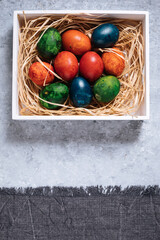Easter eggs in box with golden hay on a rustic plain grey background