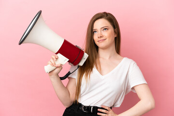 Teenager girl over isolated pink background holding a megaphone and thinking