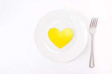 yellow heart in a plate and fork on a white background. Copy space. Place for your text.