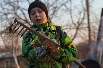 A teenage boy removes dry grass from a rake in the spring. Spring cleaning of the garden with a rake