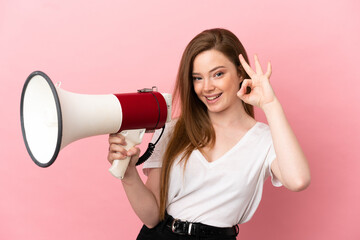 Teenager girl over isolated pink background holding a megaphone and showing ok sign with fingers
