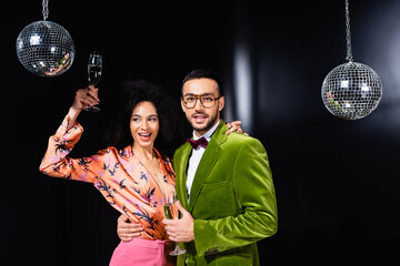 positive multiracial couple drinking champagne on black background.