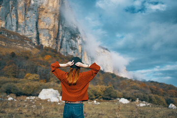 woman in a sweater and jeans with raised up arms travels in the mountains on nature landscape