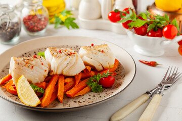 Fried pieces of cod loin, served with sweet potato fries. Light stone background.