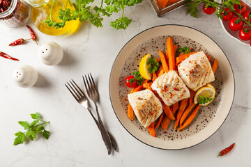 Fried pieces of cod loin, served with sweet potato fries. Light stone background.