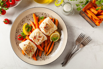 Fried pieces of cod loin, served with sweet potato fries. Light stone background.
