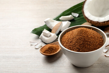 Natural coconut sugar in bowl on white wooden table, space for text