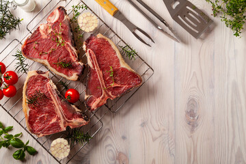 Raw t bone steak, with herbs. Grill accessories. Ready for grilling. Wooden bright background.