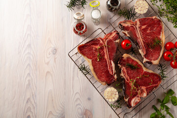 Raw t bone steak, with herbs. Grill accessories. Ready for grilling. Wooden bright background.